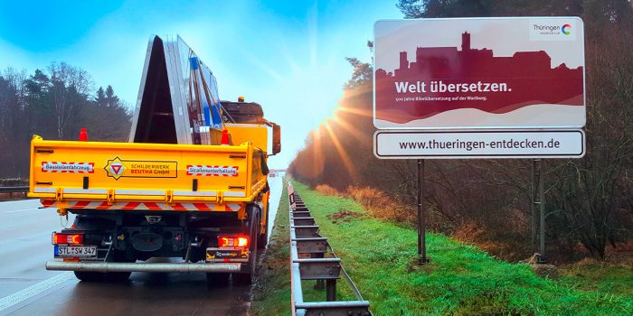 Foto einer touristischen Unterrichtstafel mit der Aufschrift: Welt übersetzen. 500 Jahre Bibelübersetzung auf der Wartburg, www.thueringen-entdecken.de Neben dem Schild befindet sich ein Baustellenfahrzeug mit neuer Folierung der Schilderwerk-Beutha GmbH