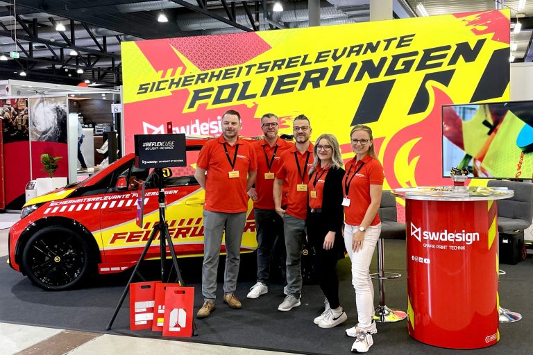 Teambild des Schilderwerk-Beutha Teams auf der FLORIAN Messe in Dresden, im Hintergrund befindet sich entsprechender Messestand mit der Aufschrift: Sicherheitsrelevante Folierungen