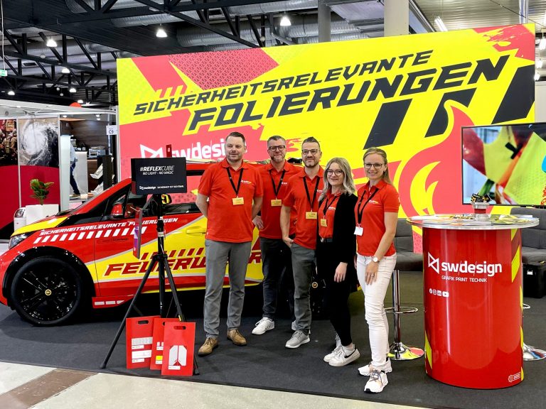 Teambild des Schilderwerk-Beutha Teams auf der FLORIAN Messe in Dresden, im Hintergrund befindet sich entsprechender Messestand mit der Aufschrift: Sicherheitsrelevante Folierungen