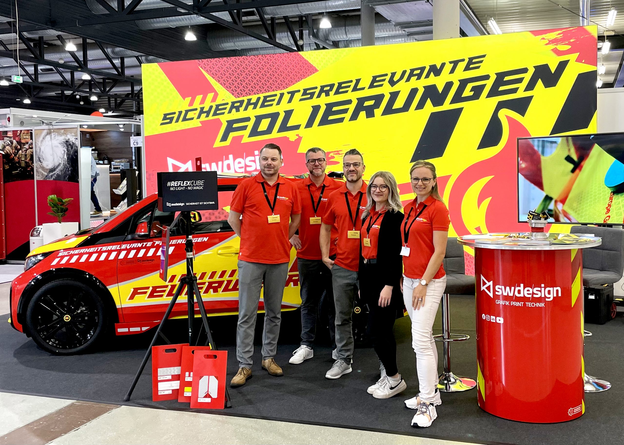 Teambild des Schilderwerk-Beutha Teams auf der FLORIAN Messe in Dresden, im Hintergrund befindet sich entsprechender Messestand mit der Aufschrift: Sicherheitsrelevante Folierungen