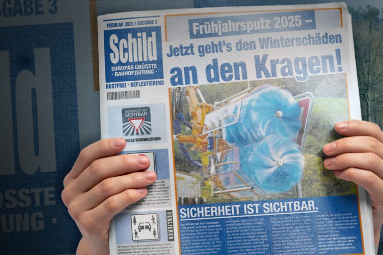 Headerbild auf der Unterseite für die SCHILD-Zeitung. Zwei Hände halten im Vordergrund die Titelseite der Ausgabe 3 der SCHILD-Zeitung. Im Hintergrund links ist hinter einem dunkeln Farbverlauf der Name der Zeitung, SCHILD als optisches Element versteckt. Auf der rechten Seite sieht man ein Vorfahrt beachten Schild mit einem Hinweisschild auf einen Kreisverkehr darunter vor einer grünen Umgebung mit einer Straße.