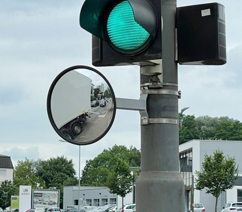 Runder Ampel-Verkehrsspiegel an einem Ampelmast, verbessert die Sicht an einer stark befahrenen Kreuzung.