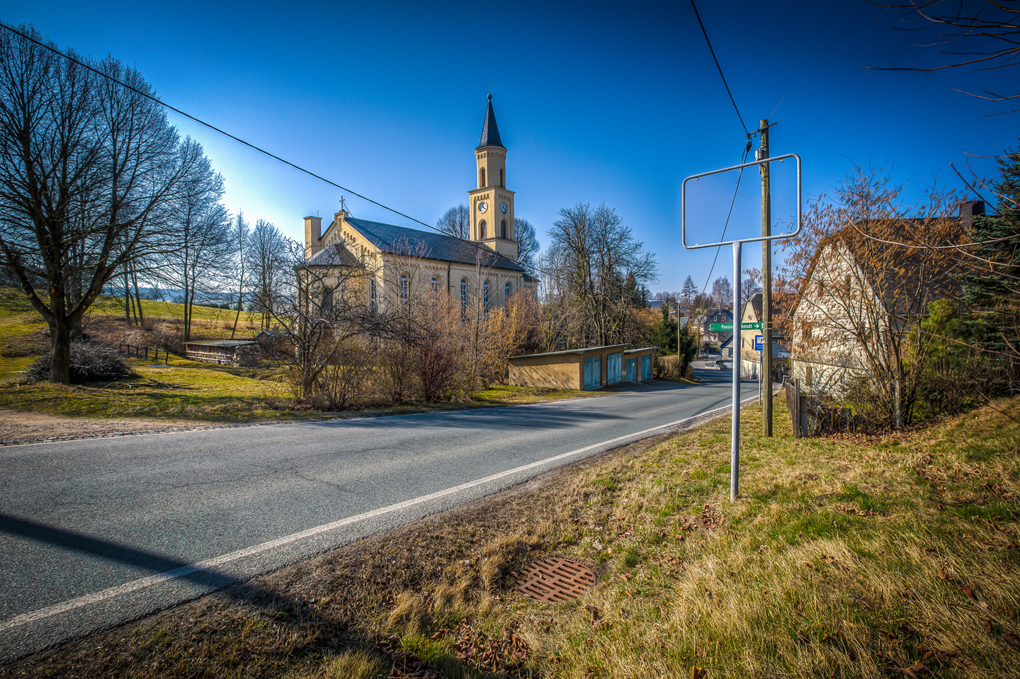 Gemeinde_Beutha_ohne Ortstafel Straße in Beutha mit Kirche im Hintergrund, umgeben von Bäumen und Häusern in einer ruhigen, ländlichen Umgebung bei sonnigem Wetter ohne Ortsschild