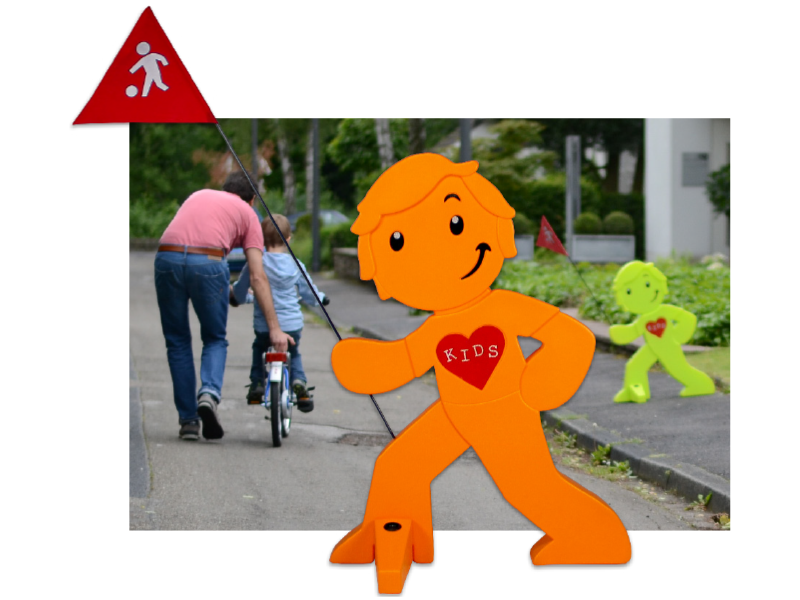 Warnaufsteller "Streetbuddy" mit Fahne vor einer Spielstraße, wo ein Vater dem Kind das Fahrradfahren beibringt.