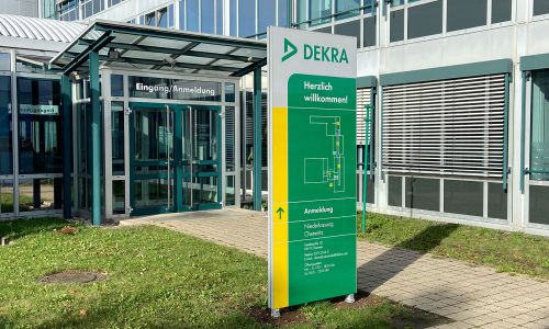 Informationsstele mit Standortübersicht vor dem Eingangsbereich eines DEKRA-Gebäudes.