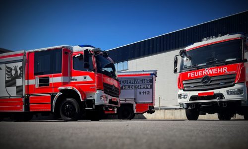 Drei Feuerwehrfahrzeuge mit individueller Fahrzeugbeschriftung und Beklebung vor einem Betriebsgebäude.