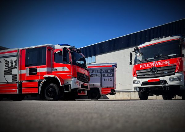 Drei Feuerwehrfahrzeuge mit individueller Fahrzeugbeschriftung und Beklebung vor einem Betriebsgebäude.