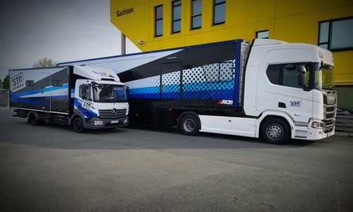 Veranstaltungsfahrzeug mit individueller Fahrzeugbeschriftung in XXL und Eventdesign vor modernem Firmengebäude.