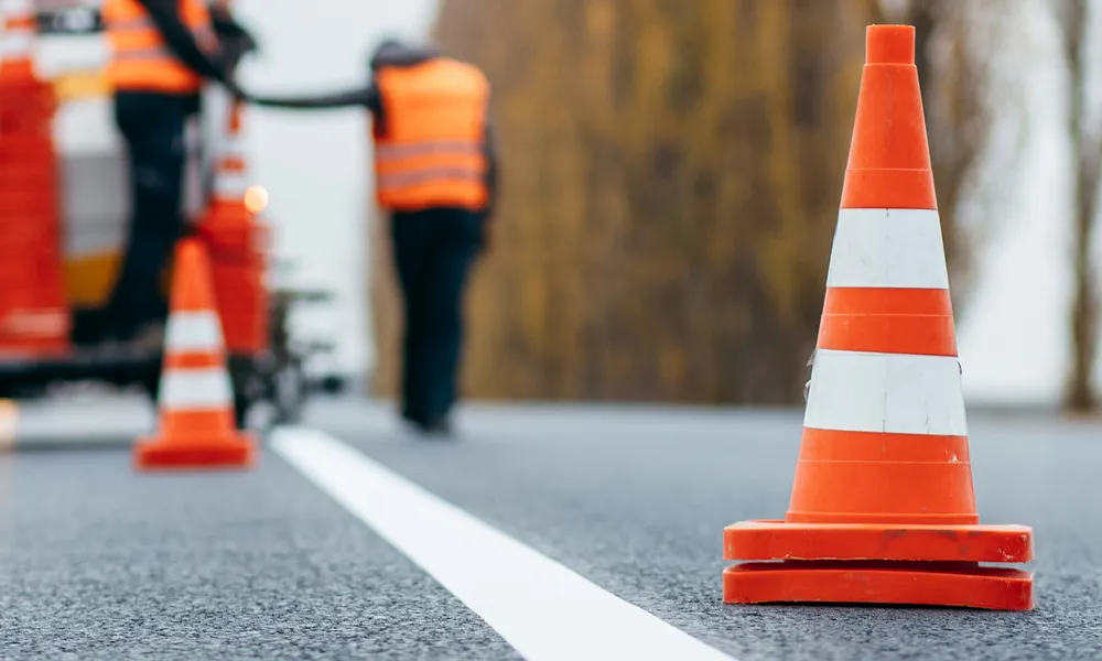 Orangefarbene Leitkegel sichern eine Fahrbahnmarkierung während Straßenbauarbeiten auf einer Straße ab.