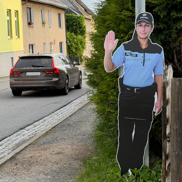 Warnfigur „Polizist“ zur Verkehrsberuhigung auf dem Schulweg in Scheibenberg Warnfigur eines Polizisten am Straßenrand in einer Ortschaft, die Autofahrer zur Geschwindigkeitsreduzierung und erhöhter Aufmerksamkeit auffordert.