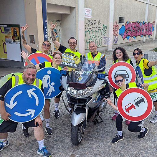 Das Schildkröten-Team des Schilderwerk Beutha posiert beim Firmenlauf Chemnitz 2026 mit großen Verkehrszeichen rund um ein Polizeimotorrad.
