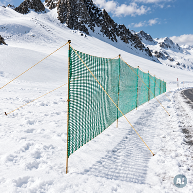 Schneezaun zum Schutz vor Schneeverwehungen an Straßen mit KI bearbeitet Grüner Schneezaun mit Abspannseilen entlang einer verschneiten Straße in einer Berglandschaft.