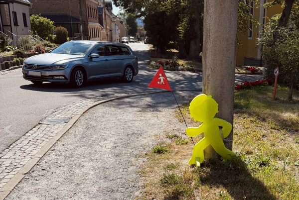 Gelber StreetBuddy mit Warnfahne am Straßenrand neben einem vorbeifahrenden Auto.